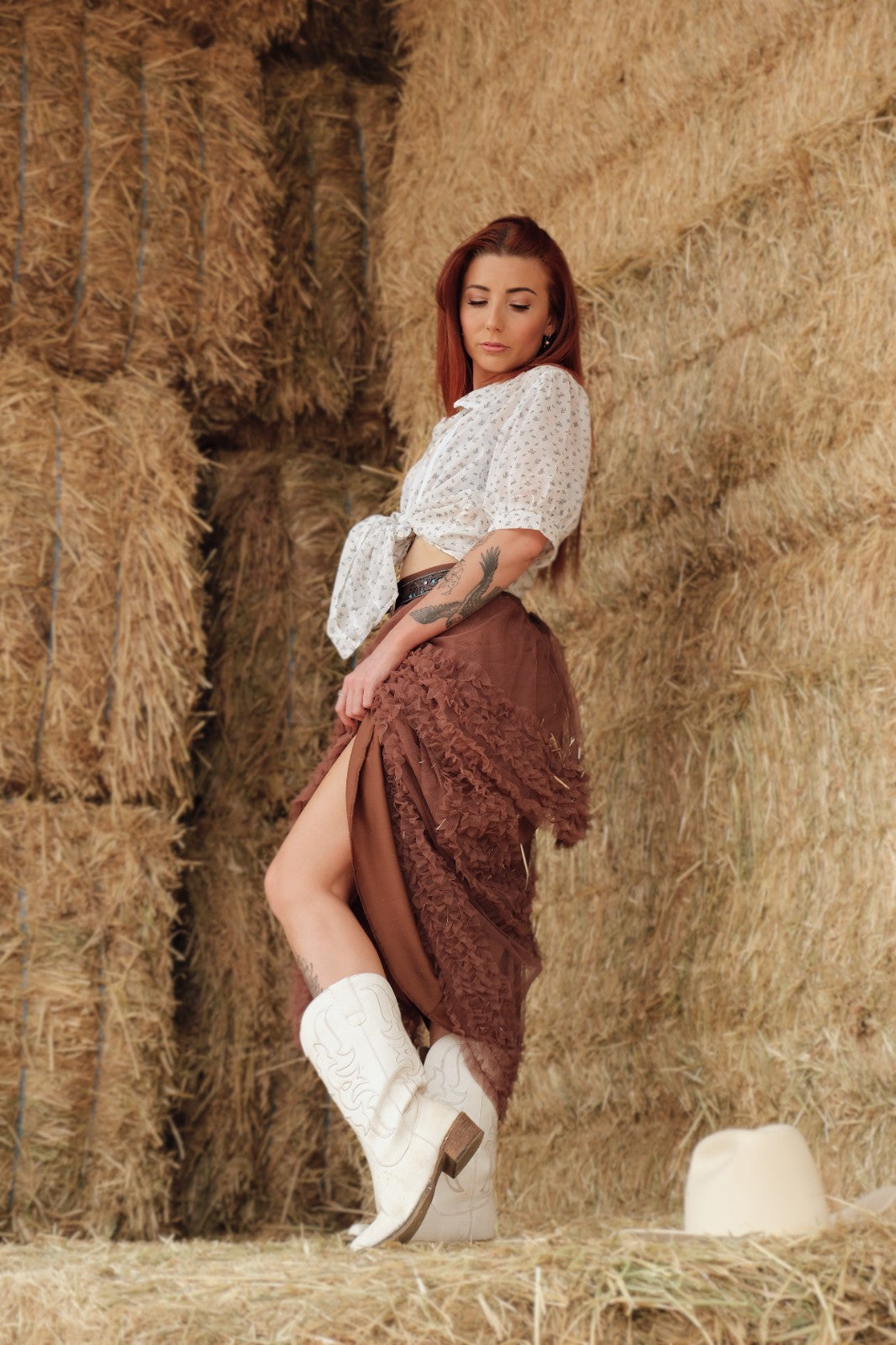 Woman in a white top and brown skirt standing among hay bales.