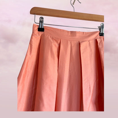 Peach-colored skirt on a wooden hanger against a pink background