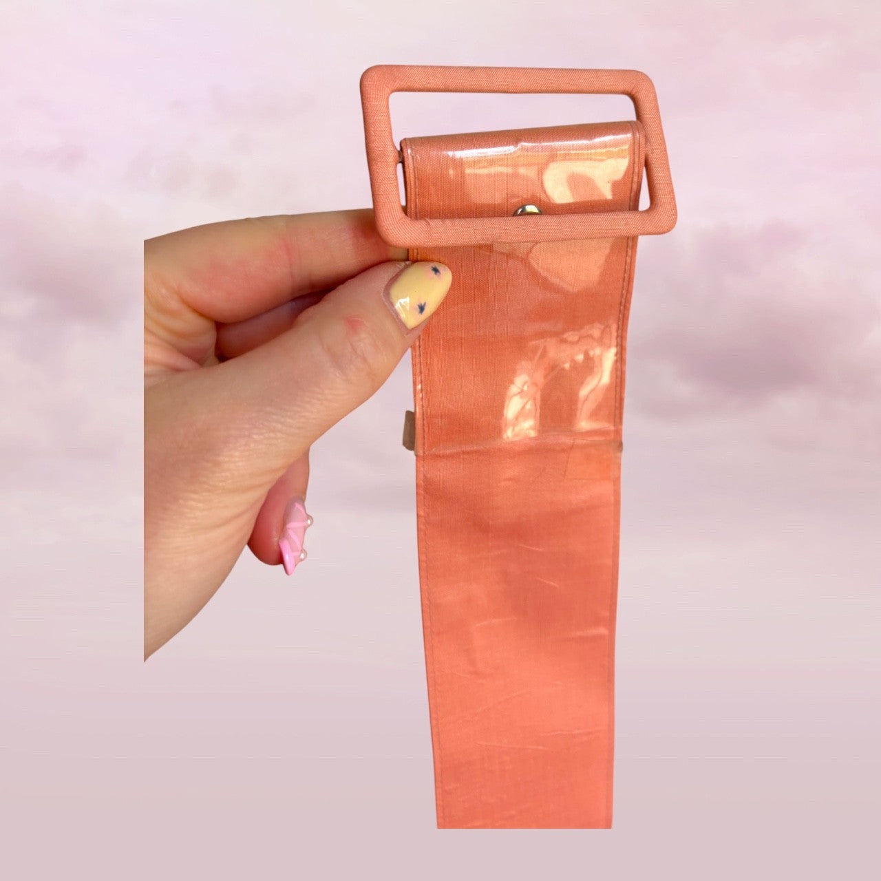 Hand holding a pink belt with a large buckle against a light pink background