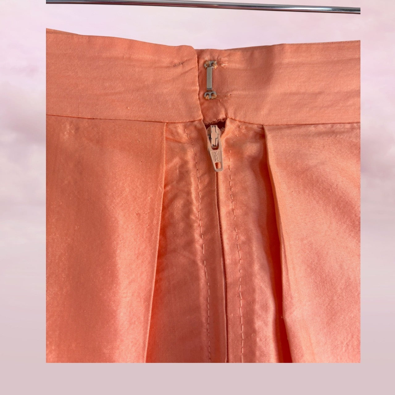Close-up of a peach-colored fabric with a zipper on a light pink background