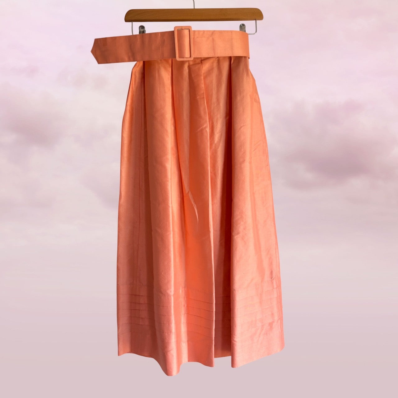 Peach-colored skirt on a hanger against a light pink background