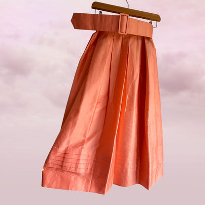 Orange skirt with a belt on a hanger against a light pink background