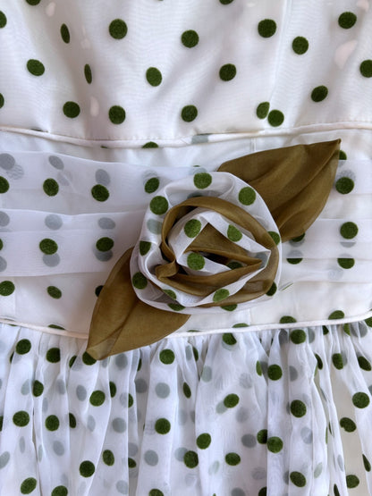 White dress with green polka dots and a floral brooch on a white background
