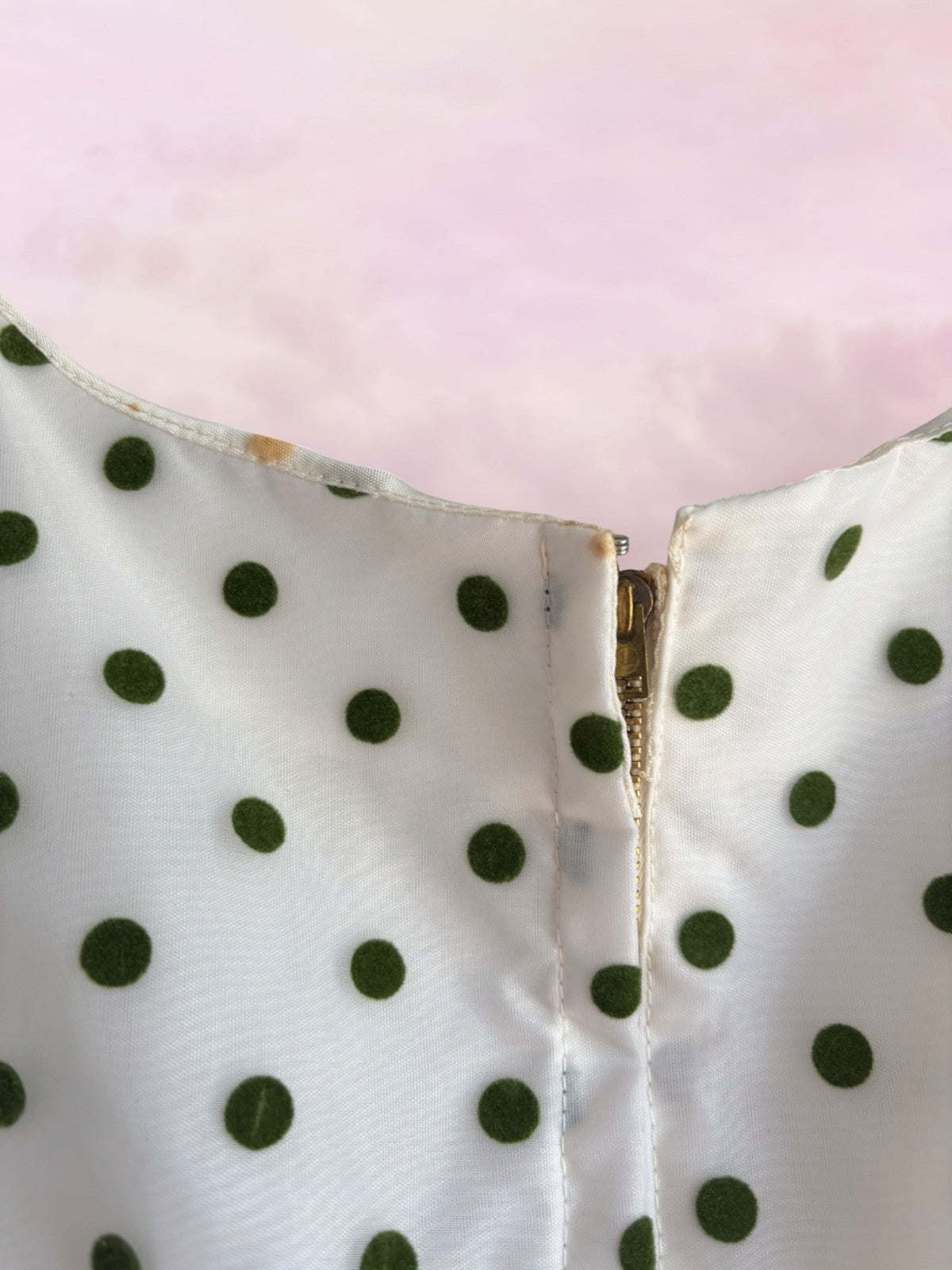 Close-up of a white fabric with green polka dots and a gold zipper on a pink background