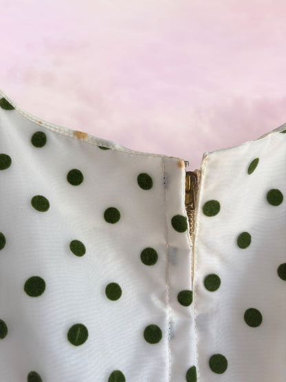 Close-up of a white fabric with green polka dots and a gold zipper on a pink background