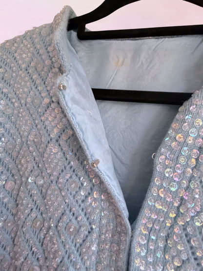 Light blue sequined garment on a hanger against a white background