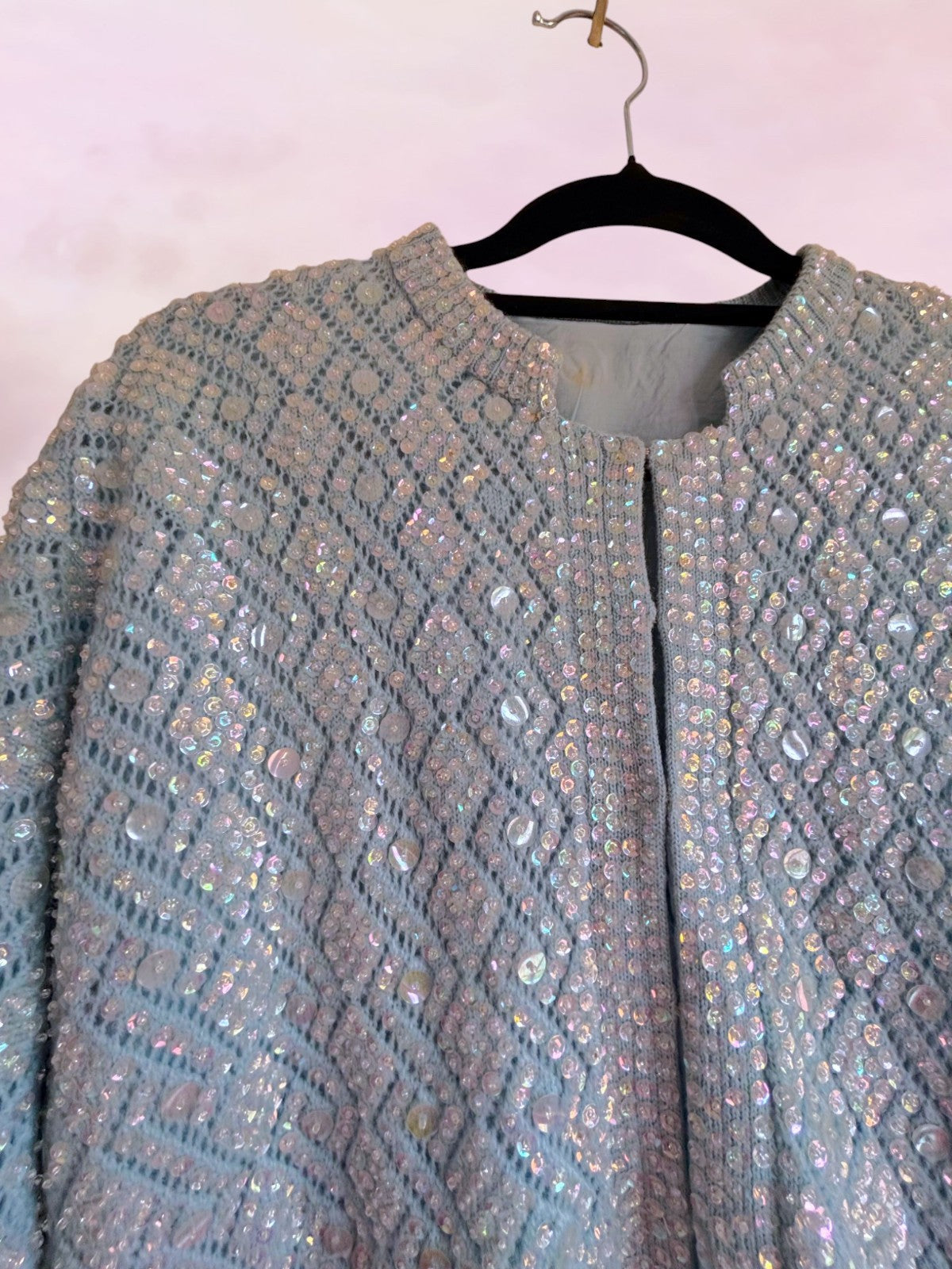 Light blue sequined jacket on a hanger against a white background