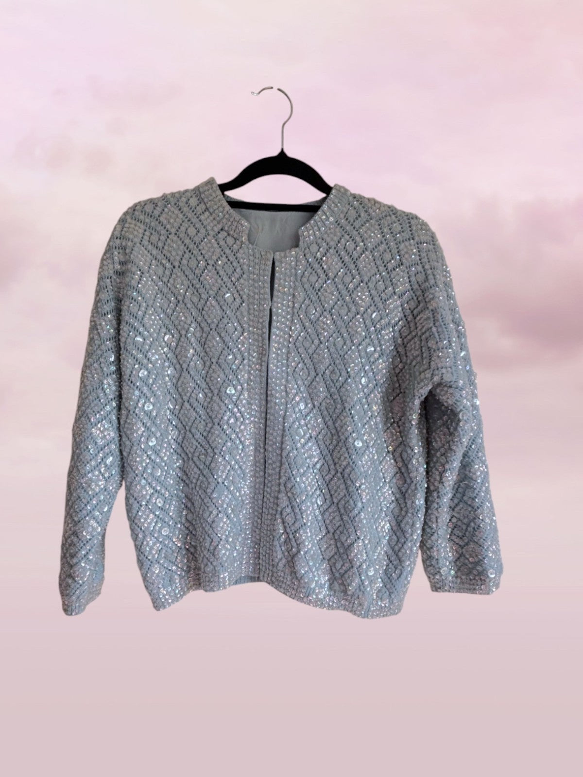 Gray textured sweater on a hanger against a pink background