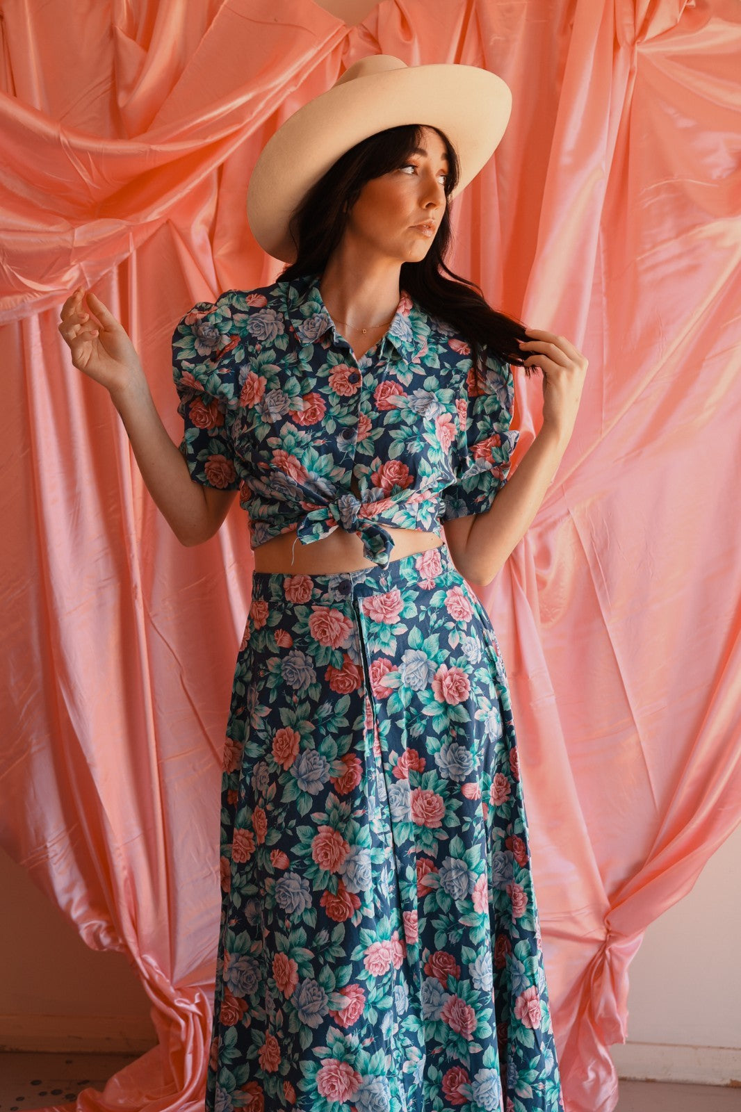 Woman wearing a floral two-piece outfit with a pink curtain background