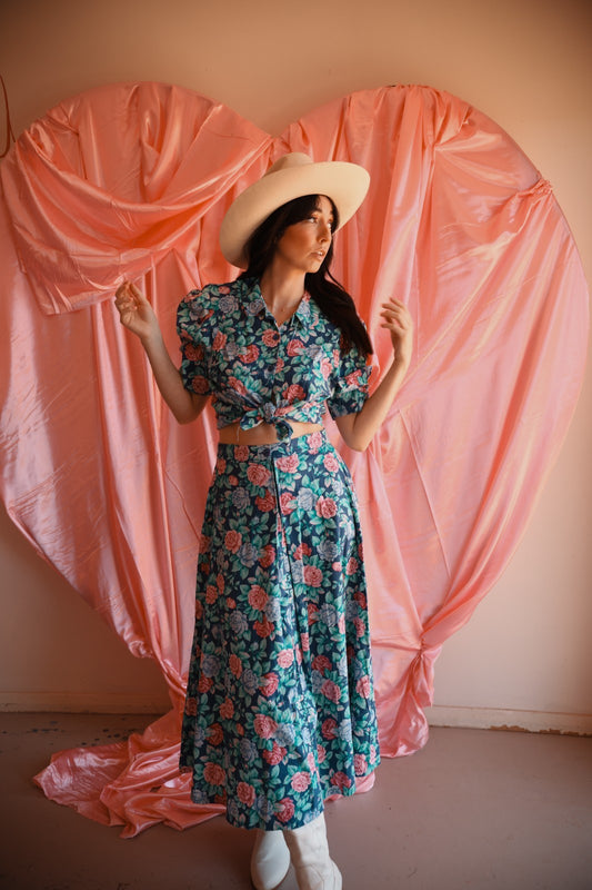 Woman in a floral dress standing in front of a heart-shaped pink curtain