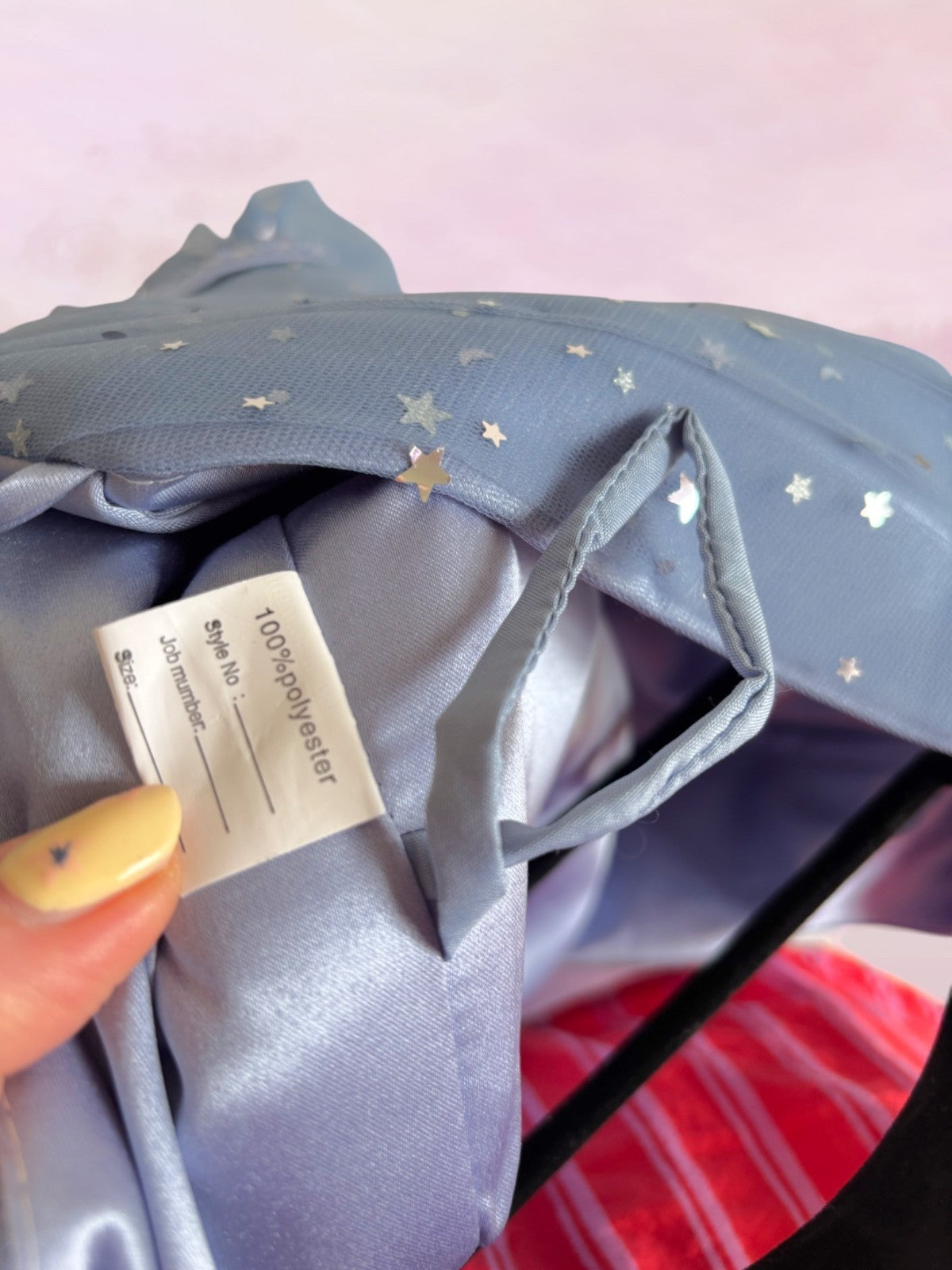 Close-up of a blue garment with a label held by a hand against a pink background