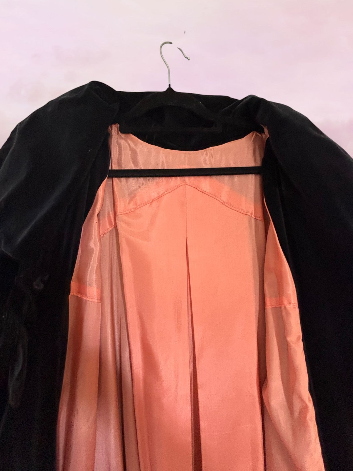 Black coat with a peach dress on a hanger against a light pink background