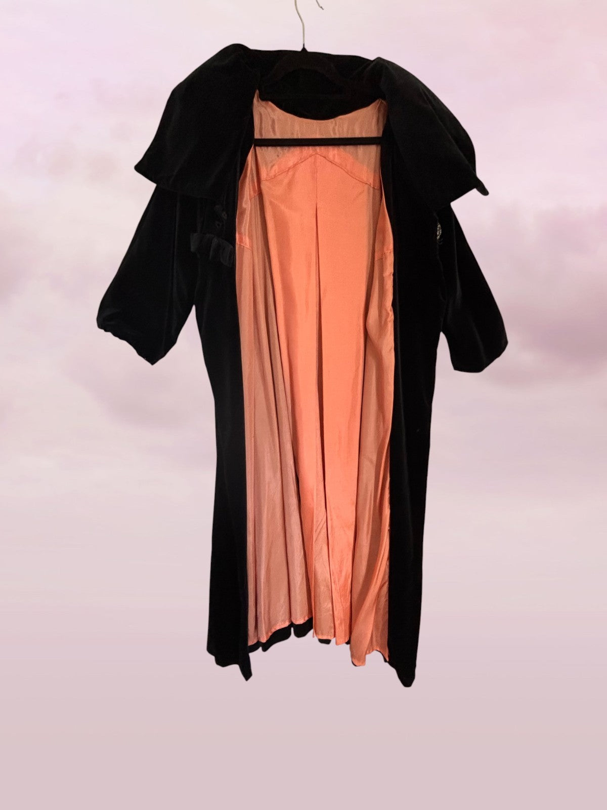 Black coat draped over a peach dress on a white background