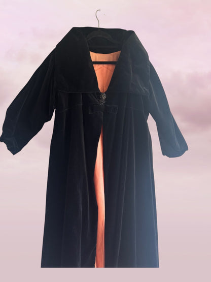 Black velvet coat with a high slit on a hanger against a light pink background