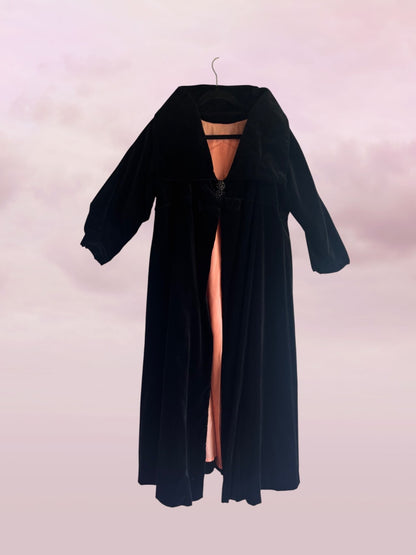 Black long coat with sheer panels on a hanger against a light pink background