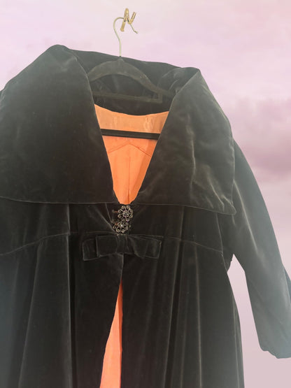 Green coat with orange lining on a hanger against a pink background