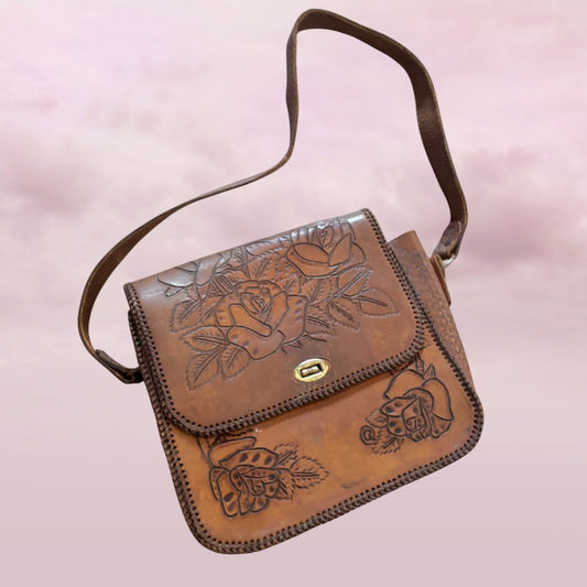 Brown leather bag with floral embossing on a light pink background
