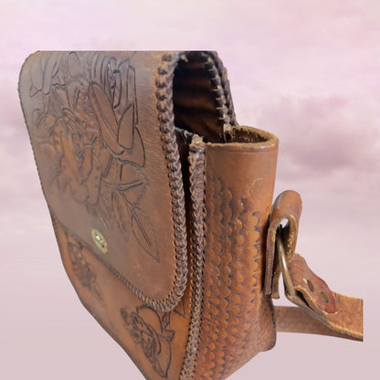 Brown leather bag with intricate designs on a light pink background
