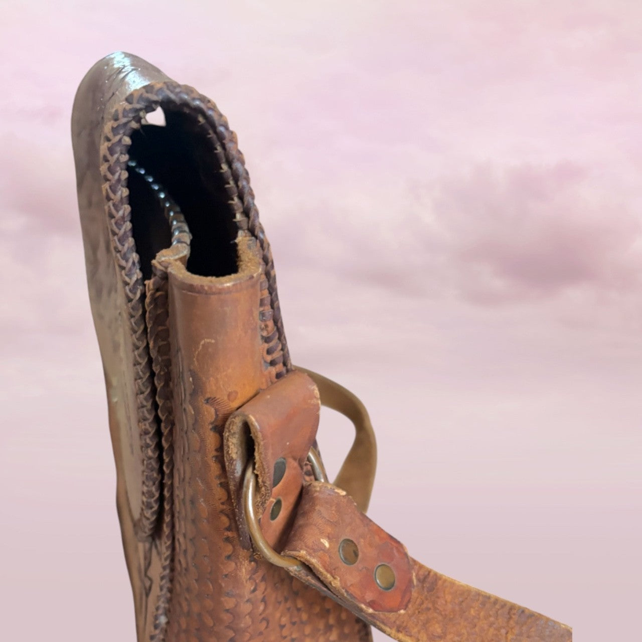 Close-up of a brown leather boot with a strap on a pink background