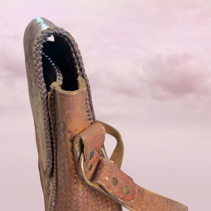 Close-up of a brown leather boot with a strap on a pink background