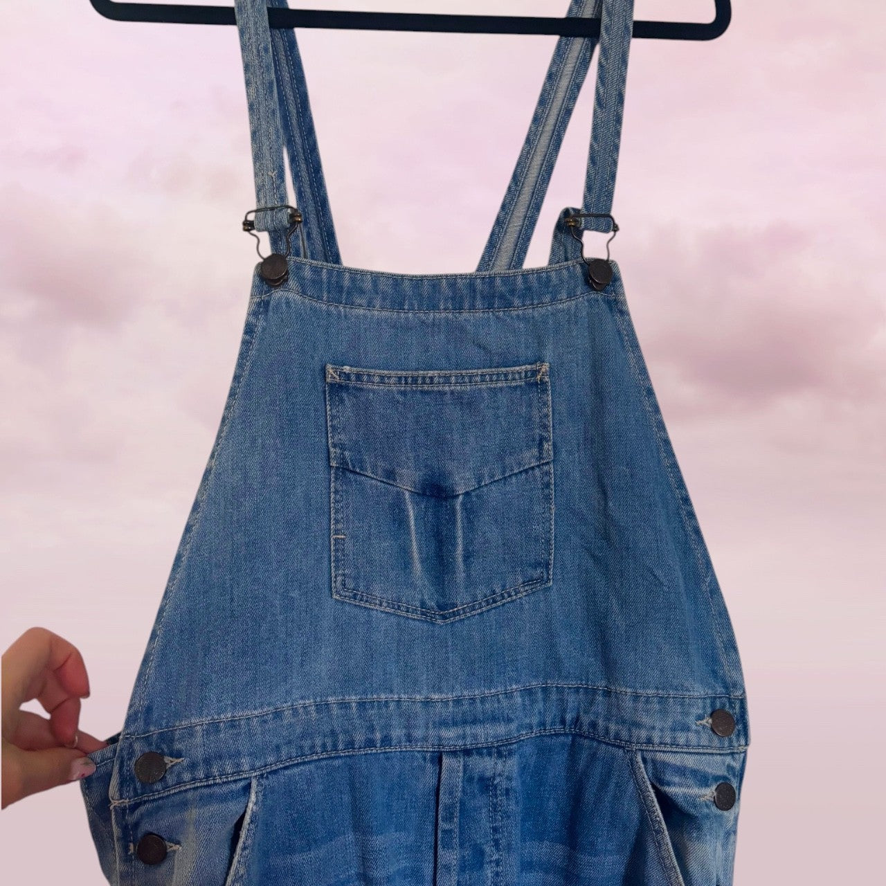Zara preloved Blue distressed denim overalls on a hanger  close up of top half against a light pink background