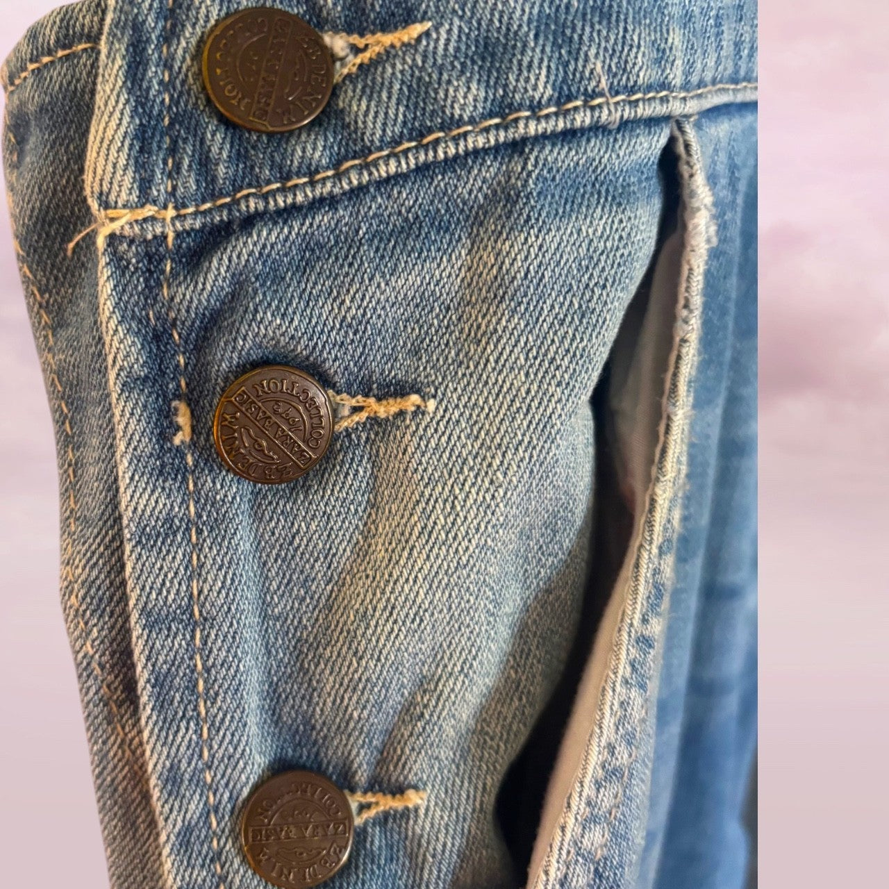 Close-up of a Zara denim overalls metal buttons on a light pink background