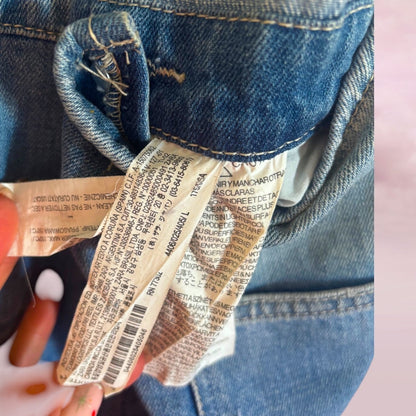 Close-up of preloved Zara denim overalls  brand label held by a hand.